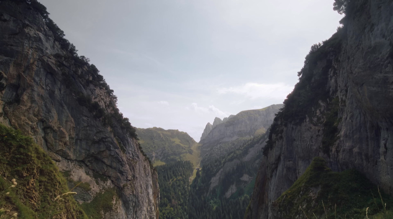 a narrow river surrounded by mountains under a cloudy sky