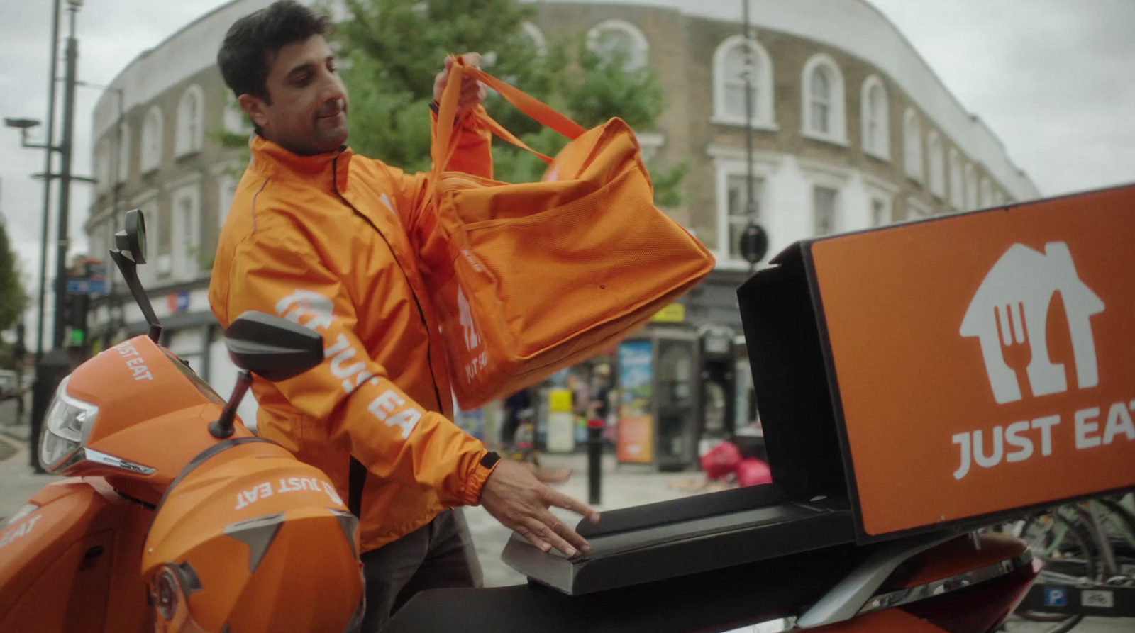 a man in an orange jacket standing next to a motor scooter