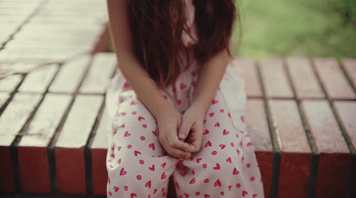 a girl sitting on a bench with her hands on her knees