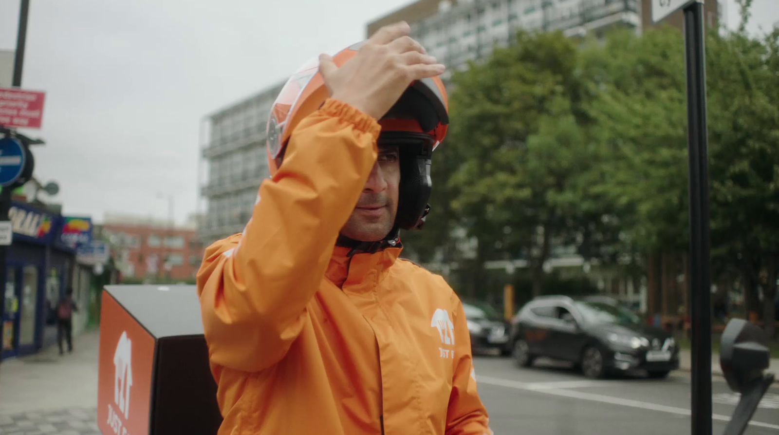 a man in an orange jacket is holding his helmet over his head