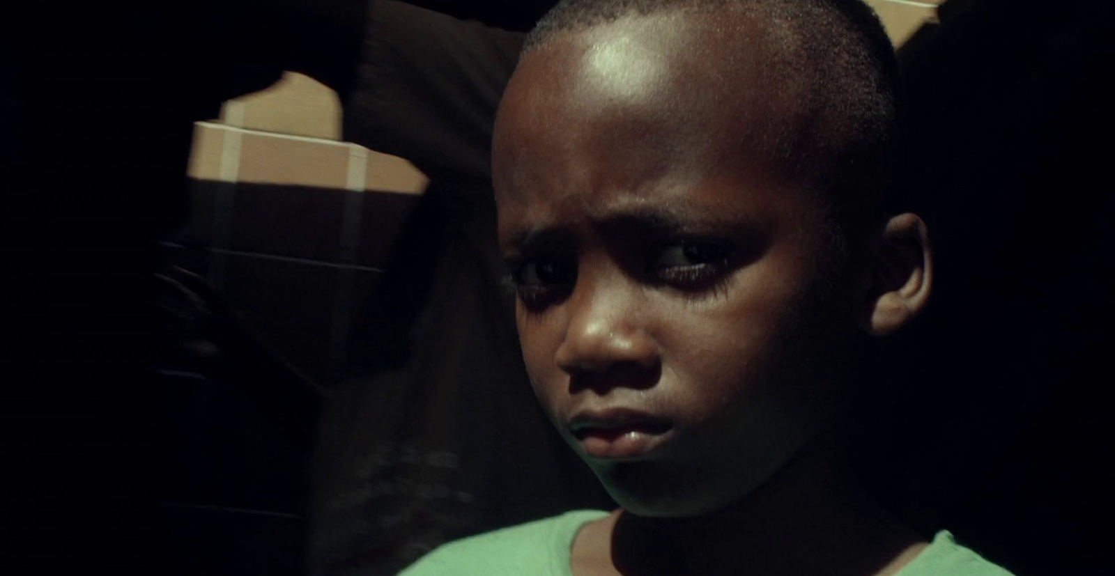 a young boy in a green shirt staring at the camera