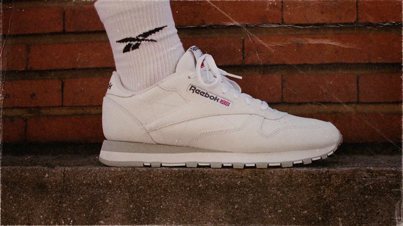 a pair of white reebok shoes sitting on top of a brick wall