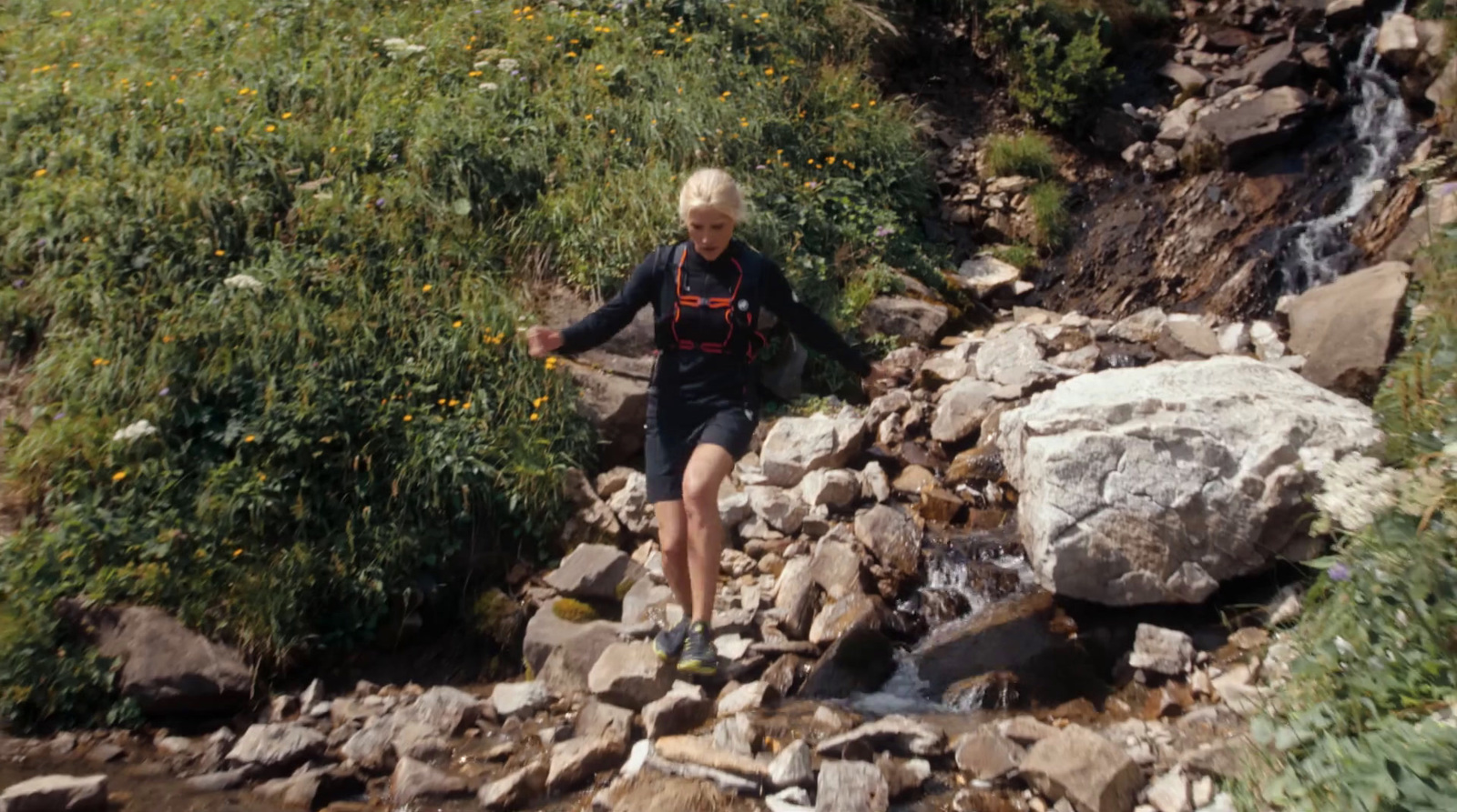 a woman hiking up a rocky trail next to a stream