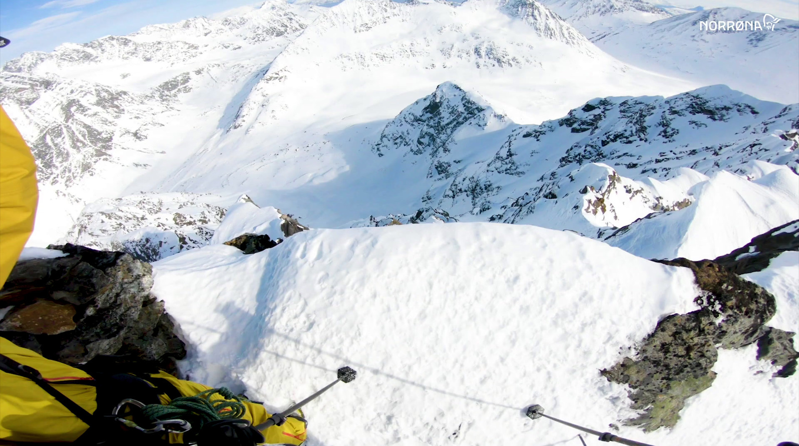 a man in a yellow jacket standing on top of a snow covered mountain