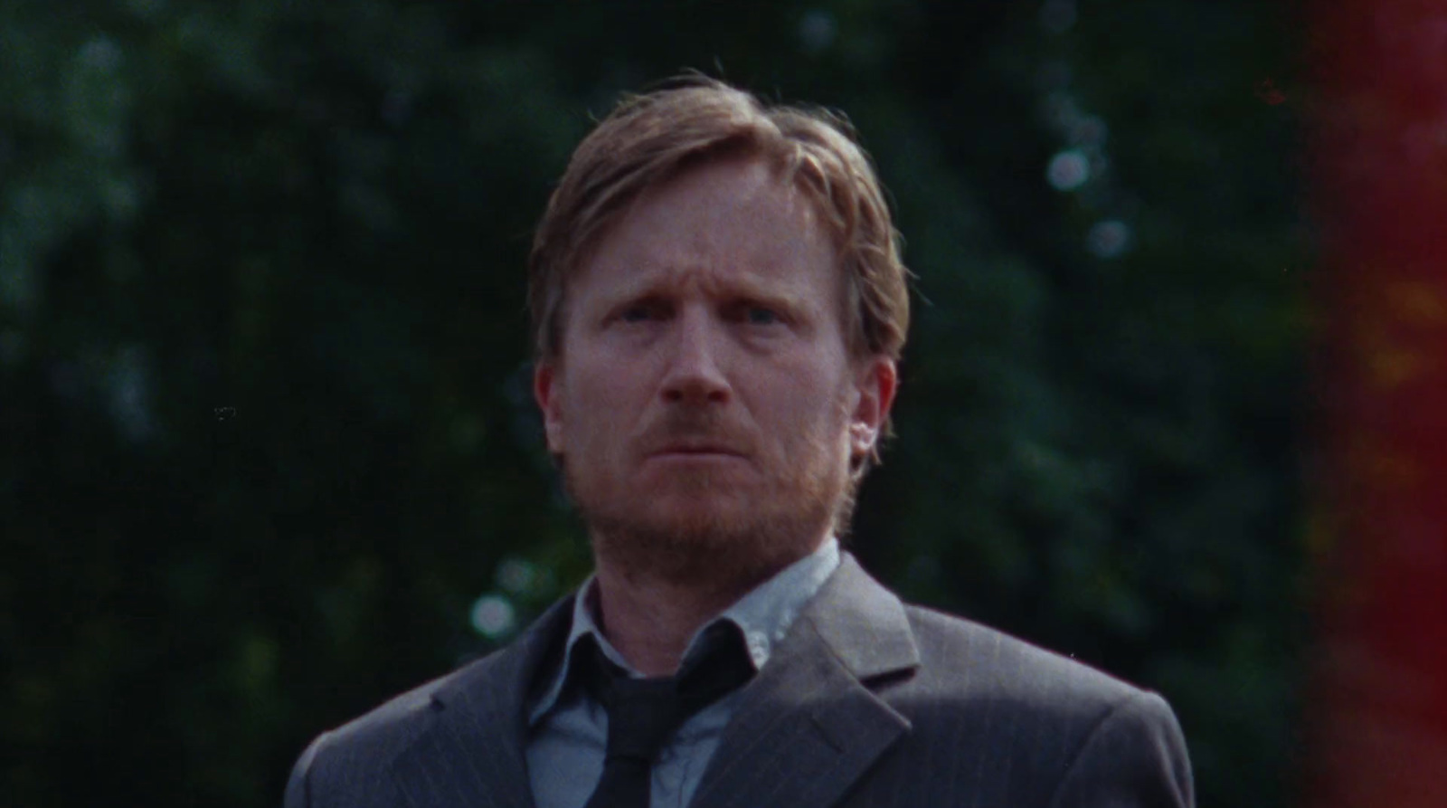 a man in a suit and tie standing in front of trees