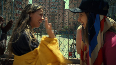 two women standing next to each other in front of a fence