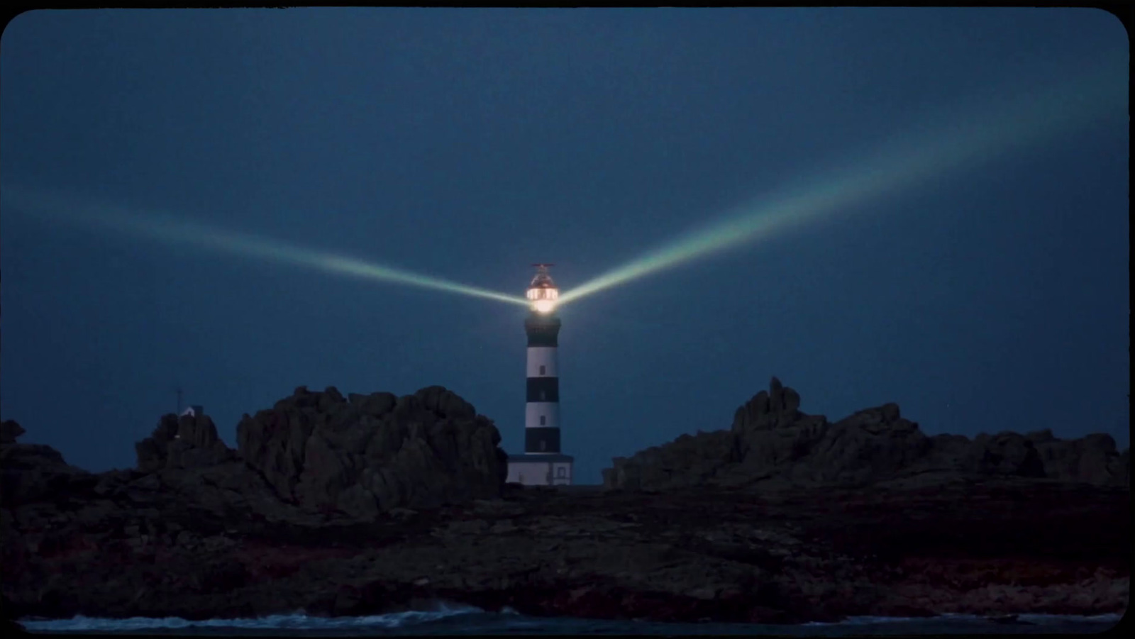 a lighthouse lit up at night on a rocky shore