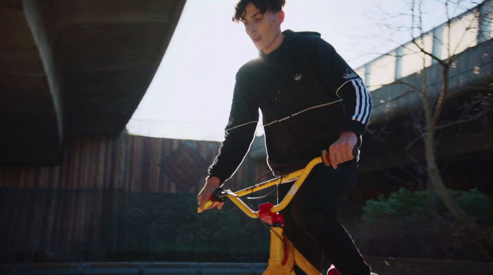 a young man riding a yellow bicycle under a bridge