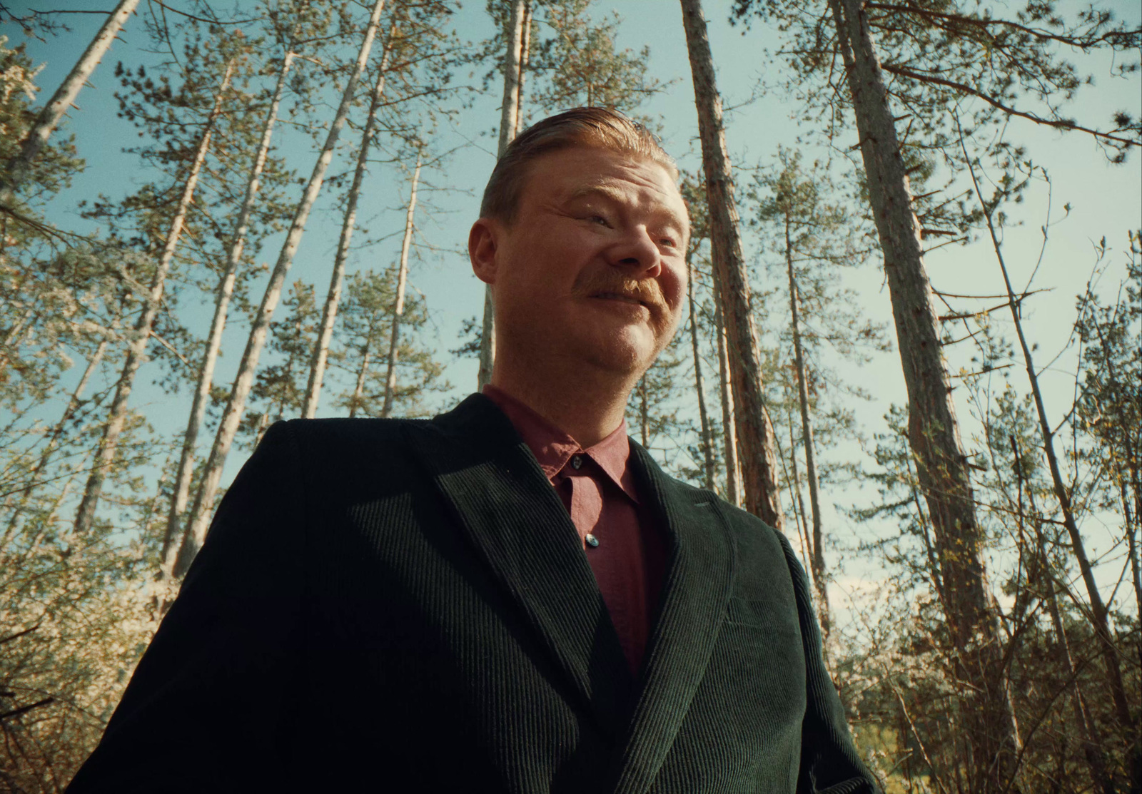 a man in a suit smoking a cigarette in the woods