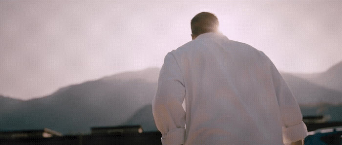 a man in a white shirt standing in front of a mountain