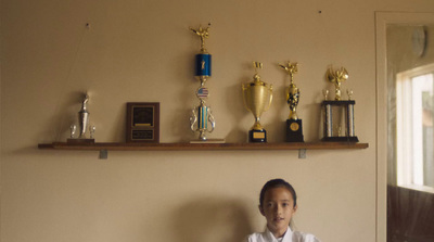 a young boy sitting in front of a shelf with trophies on it