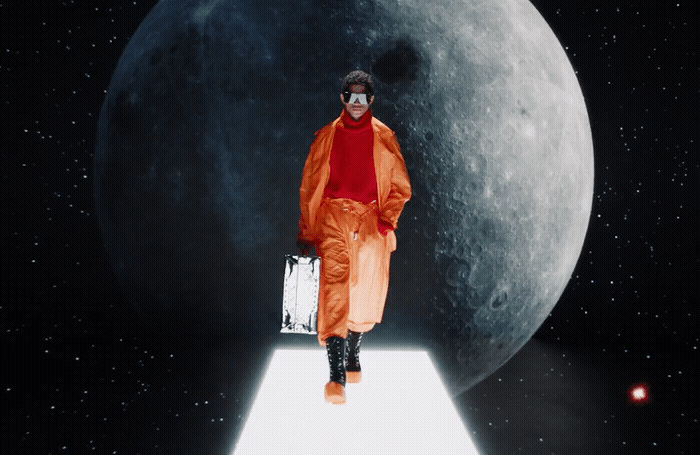 a man in an orange outfit is standing in front of the moon