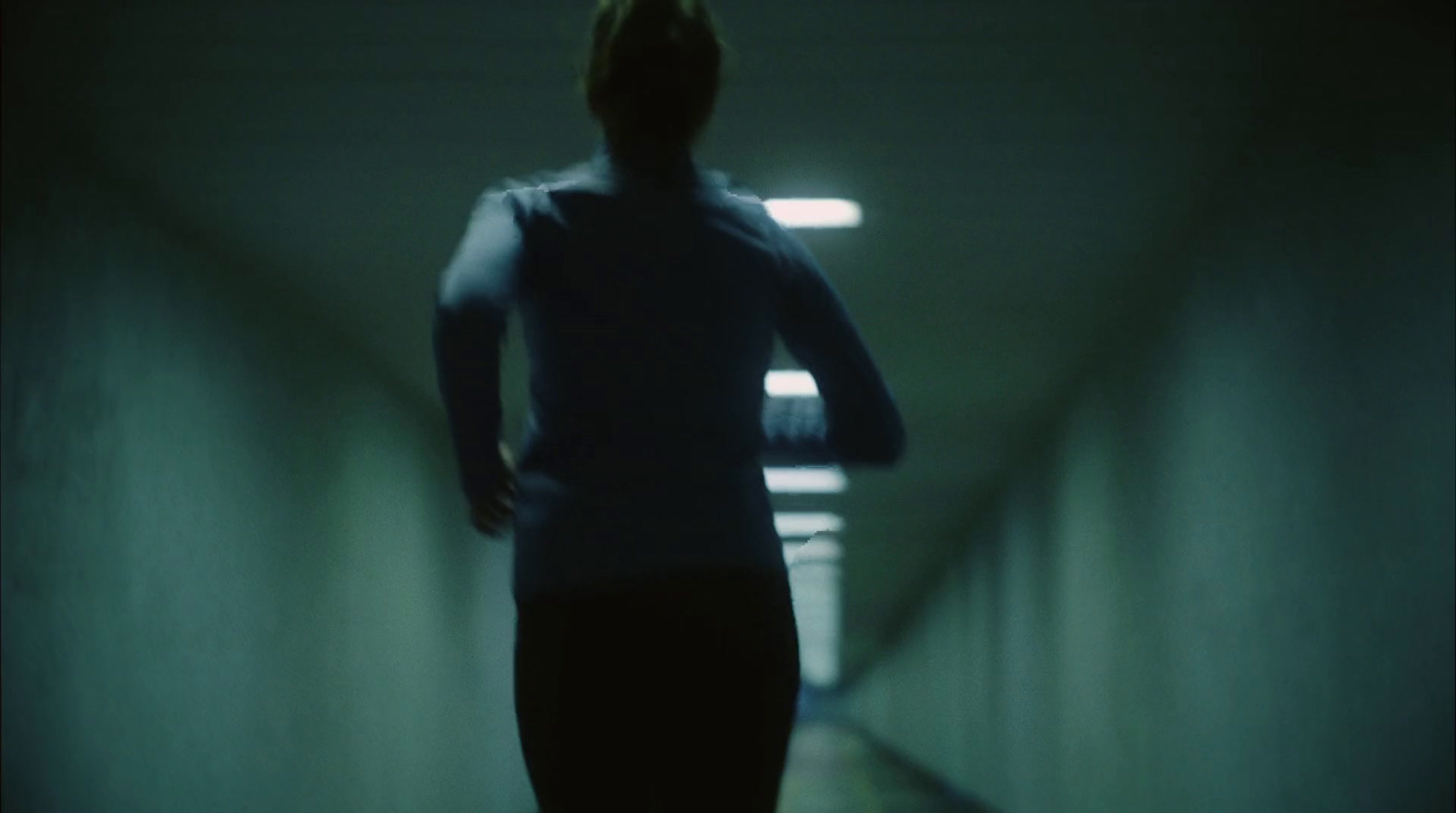 a woman is walking down a dark hallway