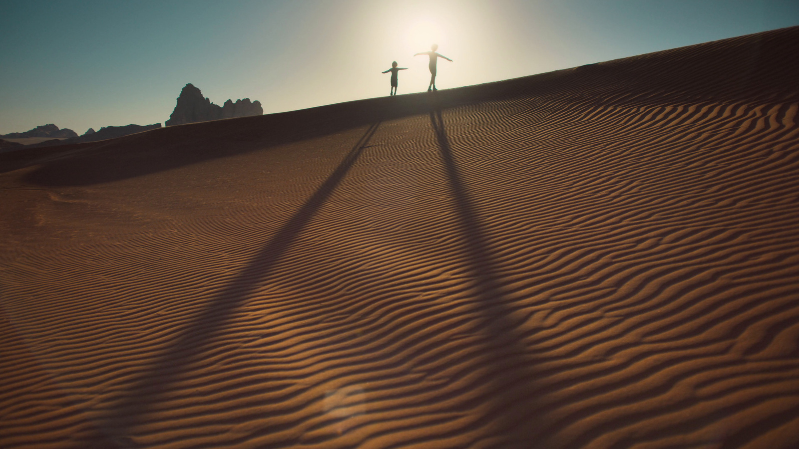 a couple of people standing on top of a sandy hill