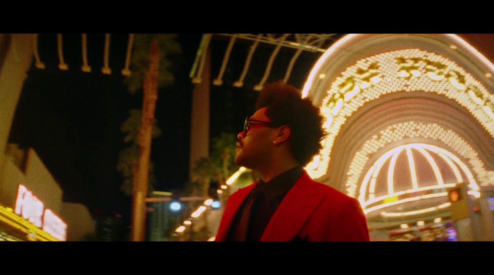 a man in a red jacket and glasses standing in front of a carnival ride