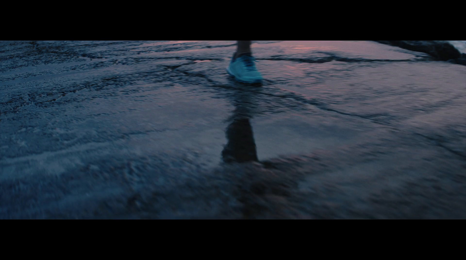 a person walking across a wet road at sunset