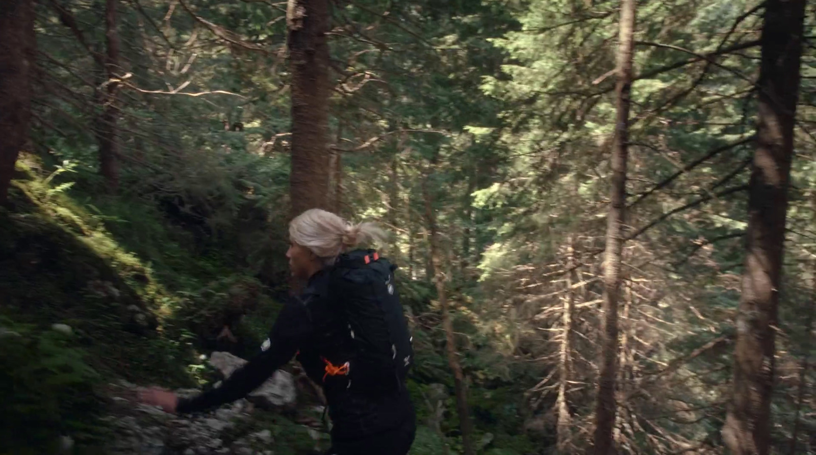 a woman walking through a forest with lots of trees