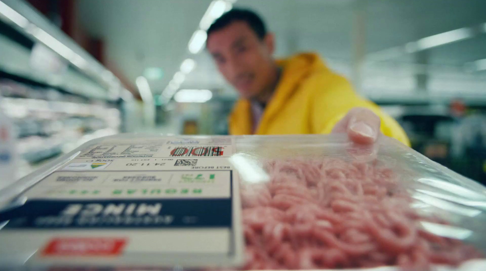 a man in a yellow jacket is looking at a package of meat