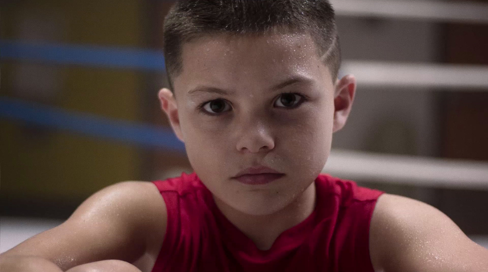 a young boy in a red shirt looking at the camera