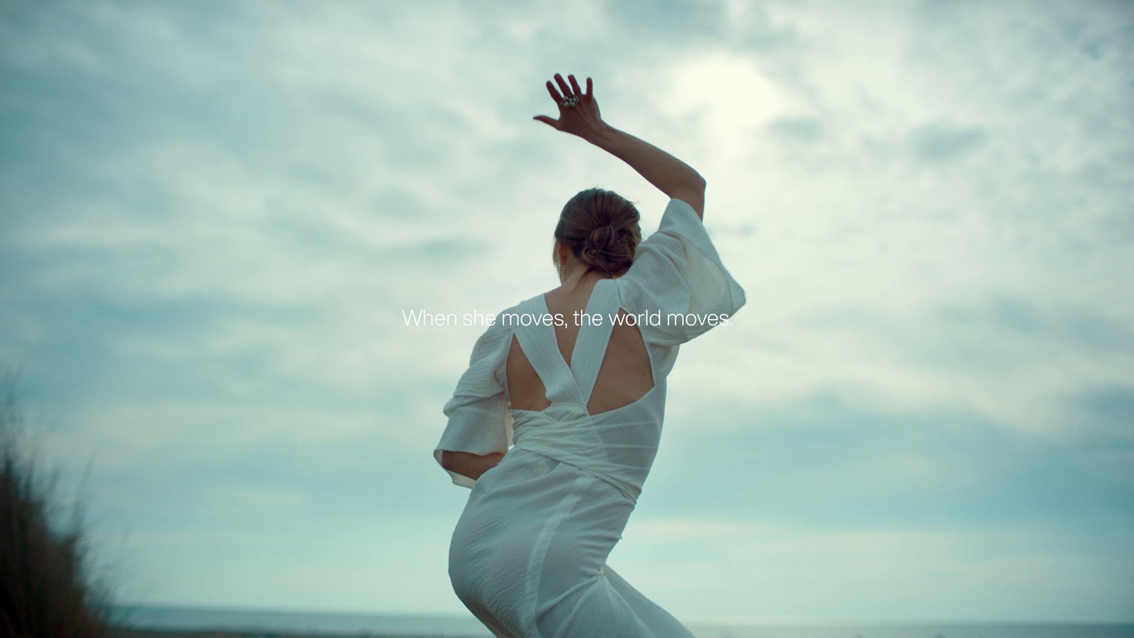 a woman in a white dress reaching up to catch a frisbee