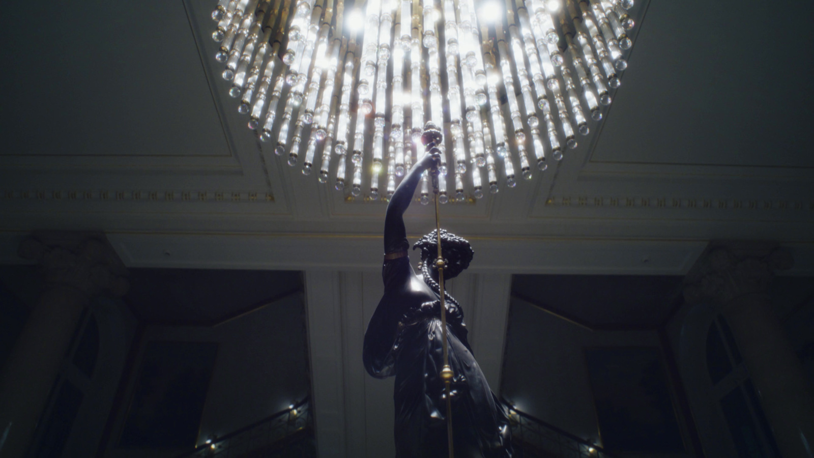 a statue of a woman reaching up to a chandelier