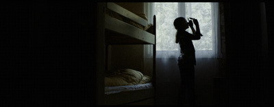 a young girl standing in a dark room next to a bunk bed