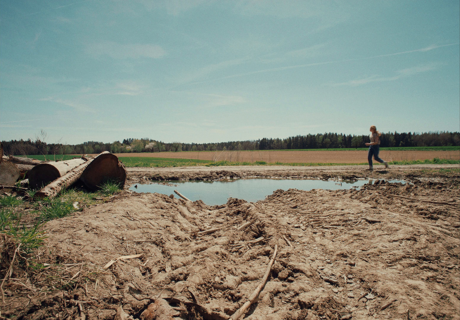 a man walking across a dirt field next to a puddle of water