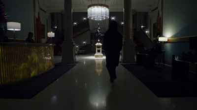 a person walking down a hall with a chandelier hanging from the ceiling