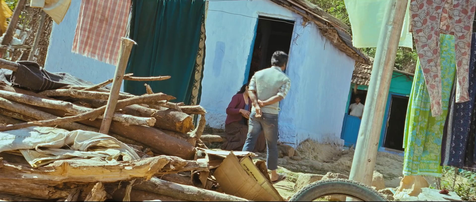 a man standing outside of a shack next to a pile of wood