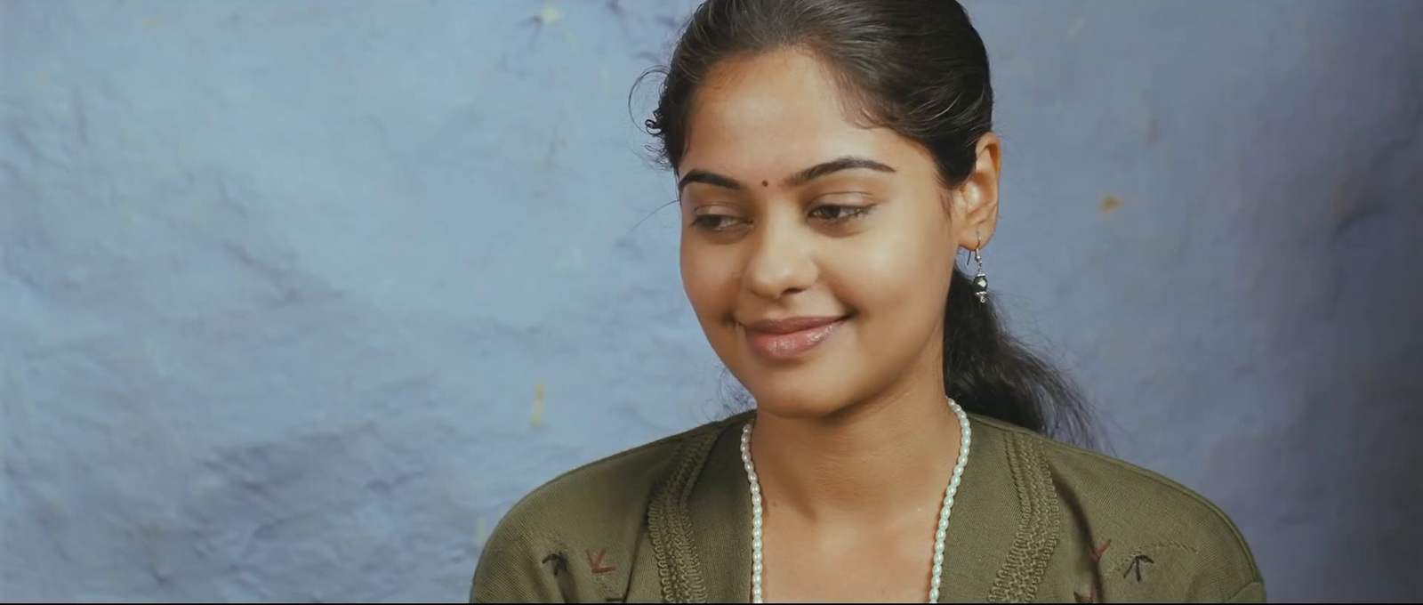 a woman with a pearl necklace and a green jacket