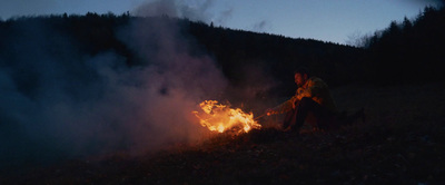 a man sitting next to a fire in a field