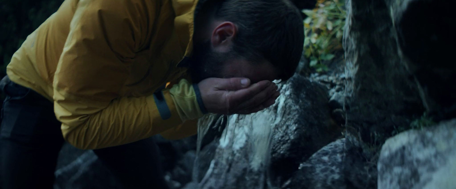 a man in a yellow jacket rubbing his face against a rock