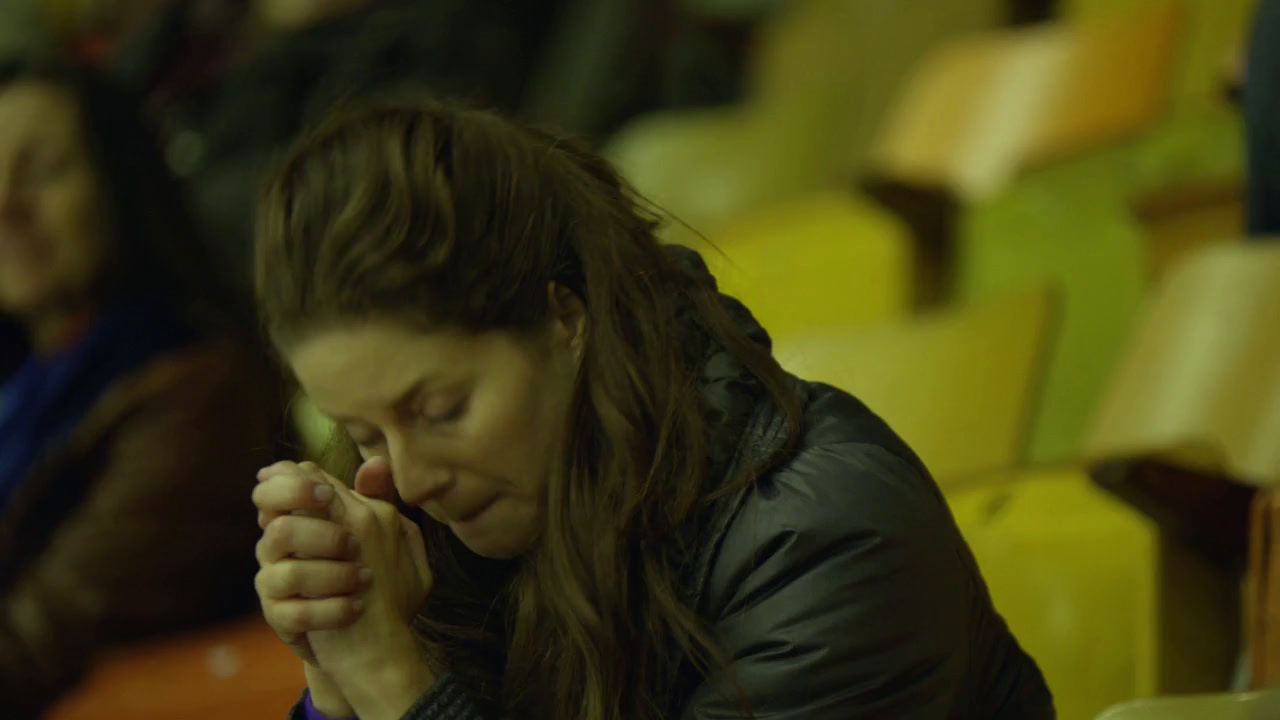 a woman sitting in a stadium holding her hands together