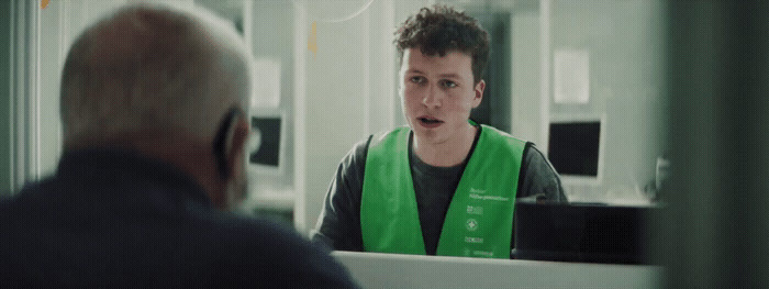 a man in a green vest talking to a man in a mirror