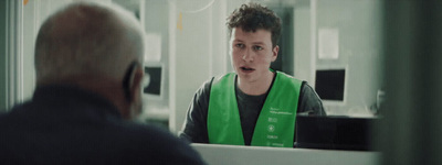 a man in a green vest talking to a man in a mirror