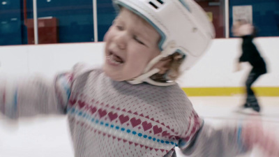 a young girl wearing a hockey helmet and skating on an ice rink