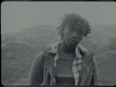 a man with dreadlocks standing in front of a mountain