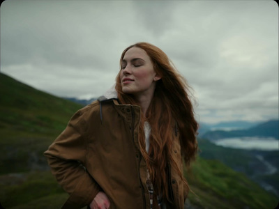 a woman with long red hair standing on a hill