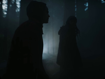 a man and a woman standing in a dark forest