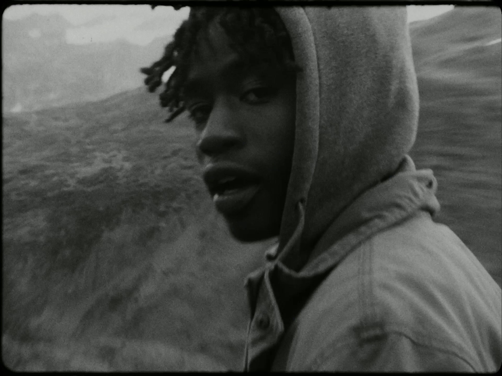 a man with dreadlocks standing in front of a mountain