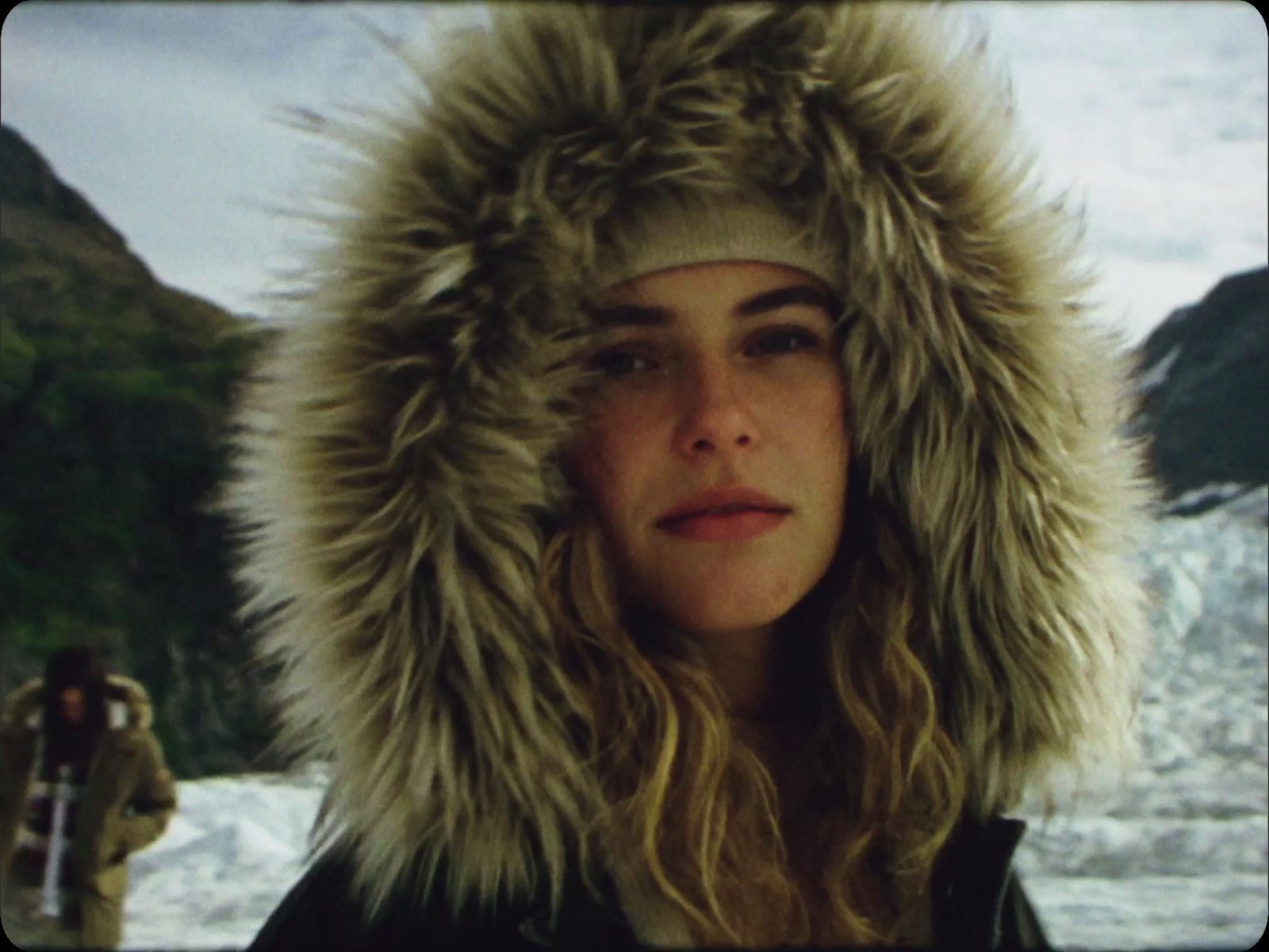 a woman wearing a fur hat in front of a glacier