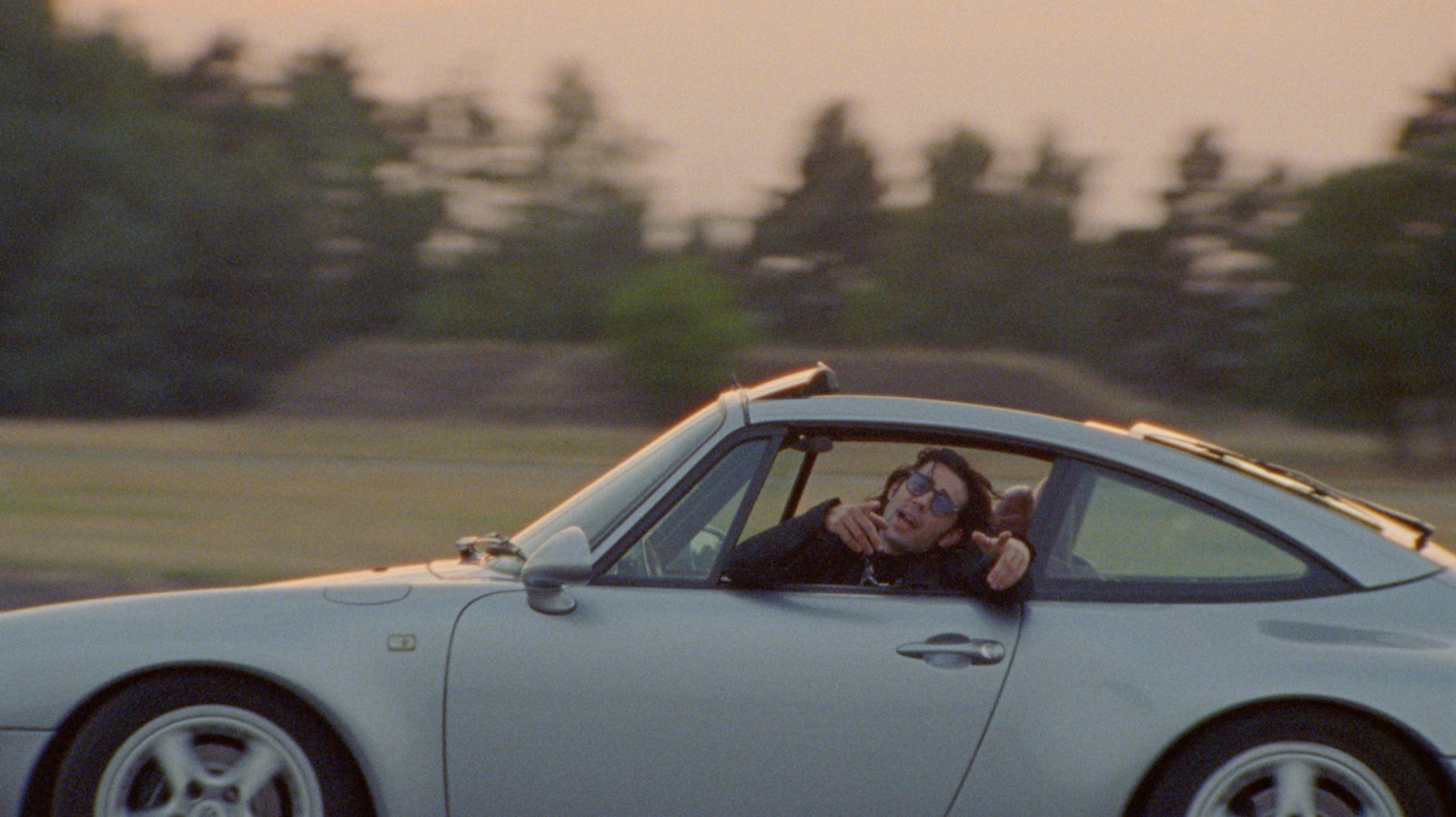 a man driving a silver sports car while talking on a cell phone