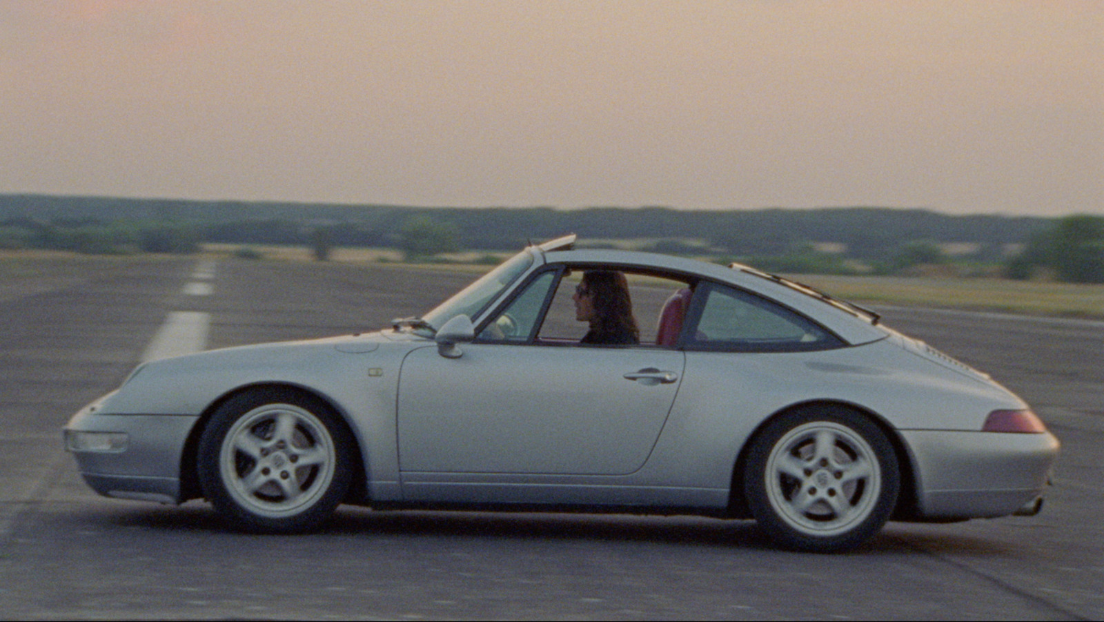 a silver car driving down a road next to a field