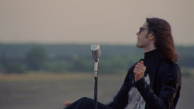 a man with long hair sitting next to a microphone