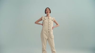 a woman in a beige jumpsuit standing with her hands on her hips