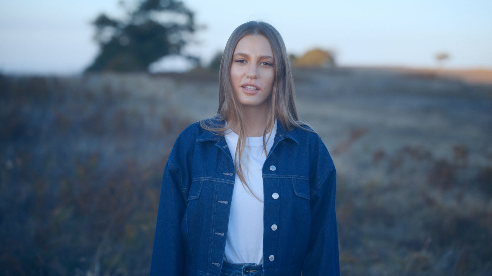 a woman in a blue jean jacket standing in a field