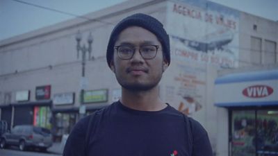 a man wearing glasses and a hat standing in front of a building