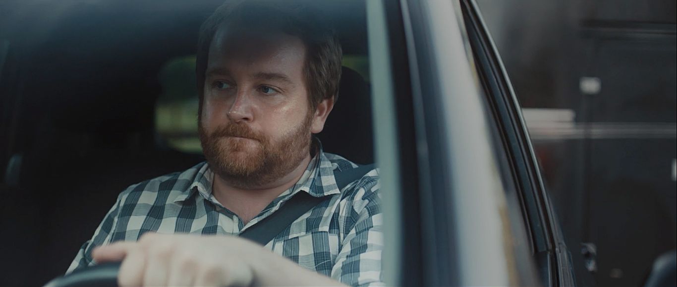 a man sitting in a car with his hand on the steering wheel