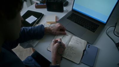 a man sitting at a desk with a notebook and a laptop