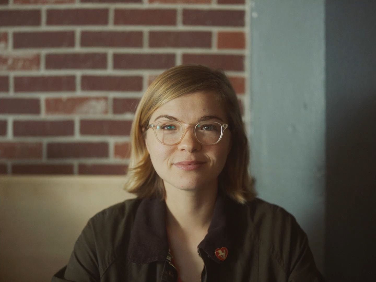 a woman wearing glasses sitting in front of a brick wall